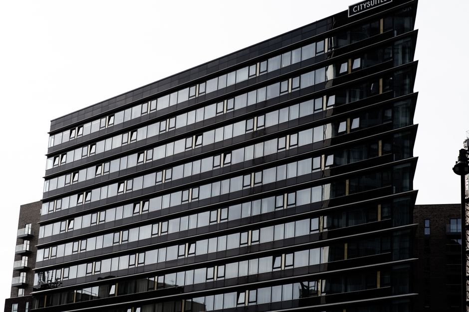 A modern multi-storey office building with a facade composed predominantly of large, reflective glass windows set within dark framing. The building's exterior features horizontal bands of black metal 