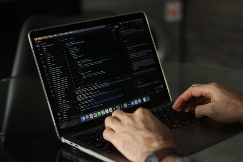 A close-up view of an open laptop with a black body on a dark surface, displaying lines of colorful code or data in shades of blue, red, and white against a blurred background. To the right of the lap